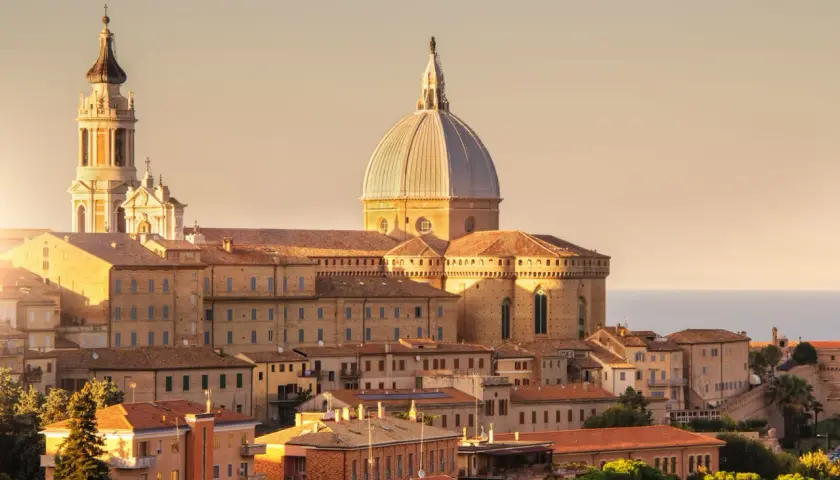 Sonnenuntergang über der Basilika von Loreto, Italien. Die Kuppel und der Glockenturm ragen über die Dächer der Stadt auf.