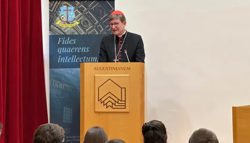 Kardinal Woelki spricht vor Zuhörern im Augustinianum. Er trägt eine schwarze Soutane und einen roten Pileolus.