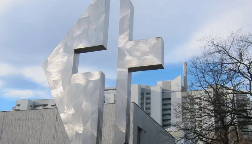 Modernes Kreuz aus gebürstetem Metall vor der Kirche St. Lukas Westkreuz.