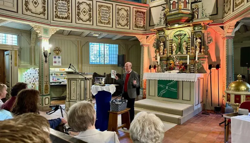 Ein Mann spricht in einer Kirche vor Zuhörern. Er hält ein Buch hoch, das von seelischem Widerstand handeln könnte.