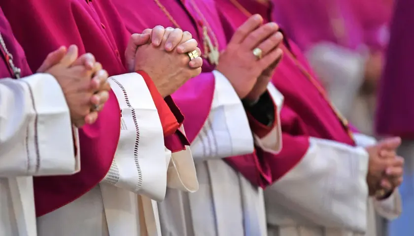 Geistliche in violetten Roben beten. Auch ein Pfarrer zahlt Kirchensteuer, wie die Ringe an den Fingern zeigen.