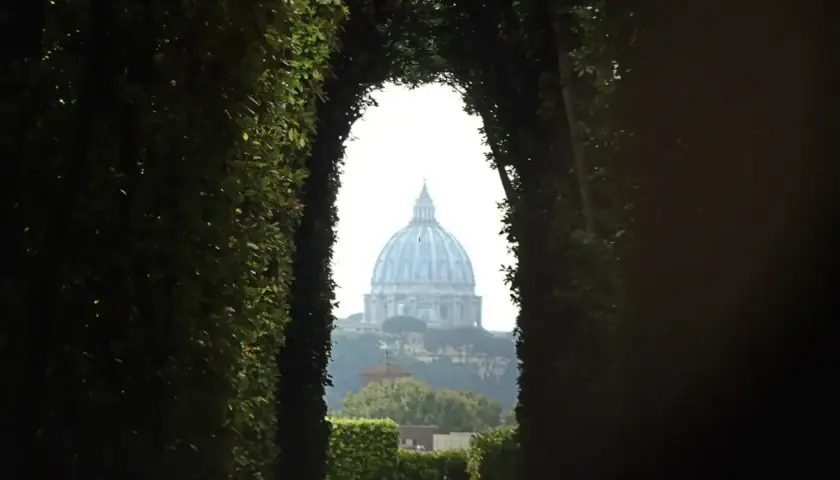 Blick durch einen grünen Torbogen auf die Kuppel des Petersdoms in Rom. Ein Ort, der an den Malteser Orden Rom erinnert.