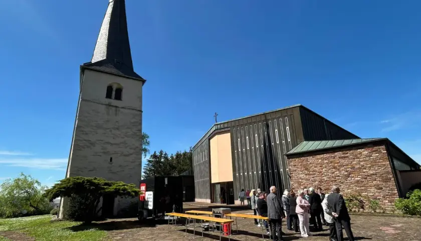 Menschen versammeln sich vor einer Kirche mit einem alten Turm. Die Frage "was ist Profanierung" könnte hier aufkommen, wenn die Kirche nicht mehr als Gotteshaus genutzt wird.