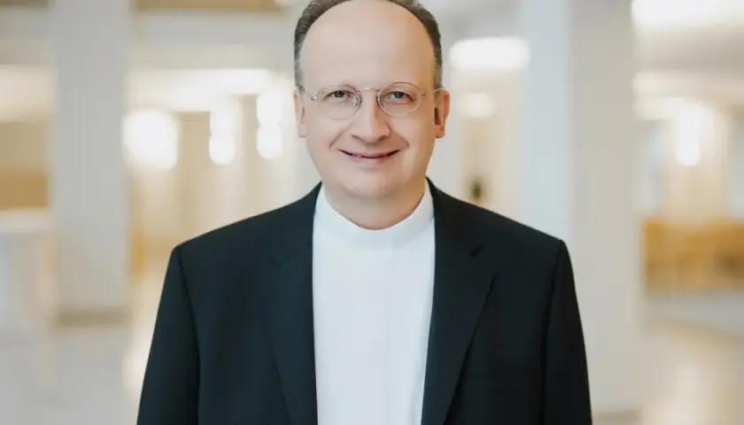 Ein Mann mit Brille trägt ein schwarzes Sakko über einem weißen Hemdkragen. Er lächelt freundlich. Er könnte ein Generalvikar sein, der die Stellvertretung des Bischofs übernimmt.