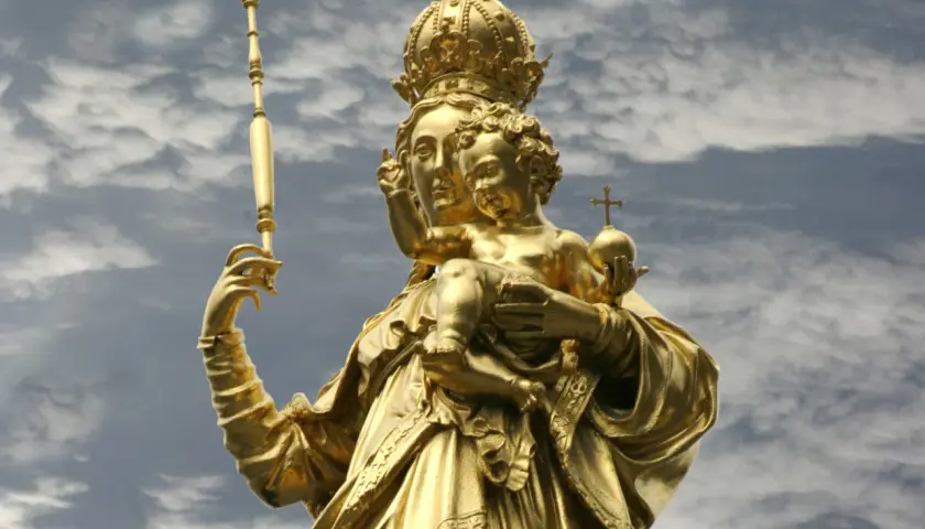 Goldene Statue der Muttergottes mit Kind, dem Patron von Bayern, vor dramatischem Wolkenhimmel.