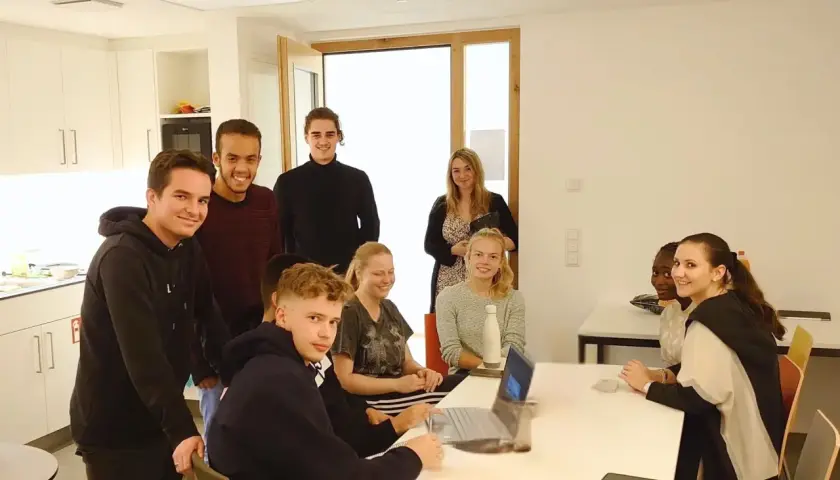 Eine Gruppe junger Leute im Sophie Barat Haus, einige lächelnd, andere am Laptop.