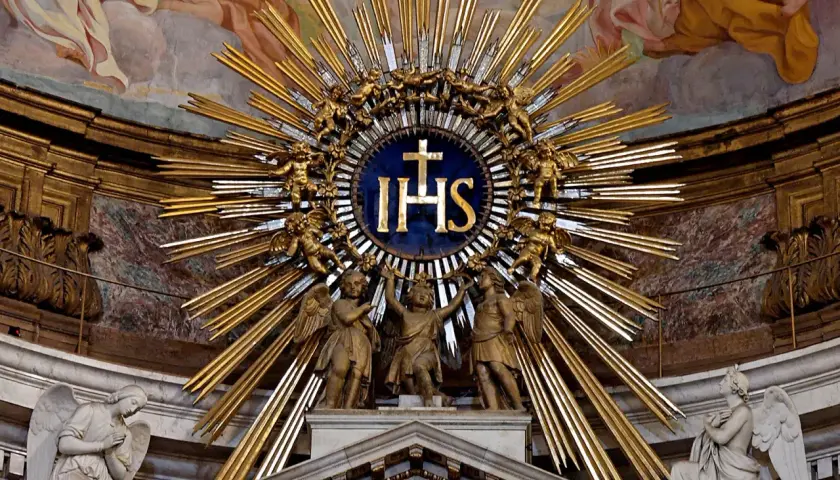 Goldene Strahlenkrone mit IHS-Monogramm, das die Bedeutung von Jesus Christus symbolisiert, umgeben von Engeln und Putten.