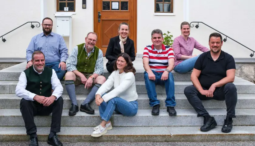 Eine Gruppe von Menschen sitzt lächelnd auf einer Treppe. Sie scheinen Teil einer Gemeinschaft zu sein, vielleicht ein Dekanat, das sich für ein Foto versammelt hat.