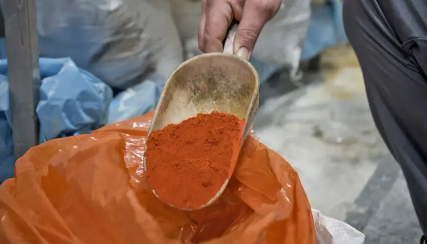 Eine Schaufel mit leuchtend orangefarbenem Pulver wird über einen orangefarbenen Beutel gehalten. Die Farben und ihre Bedeutung sind Teil eines alten Handwerks.