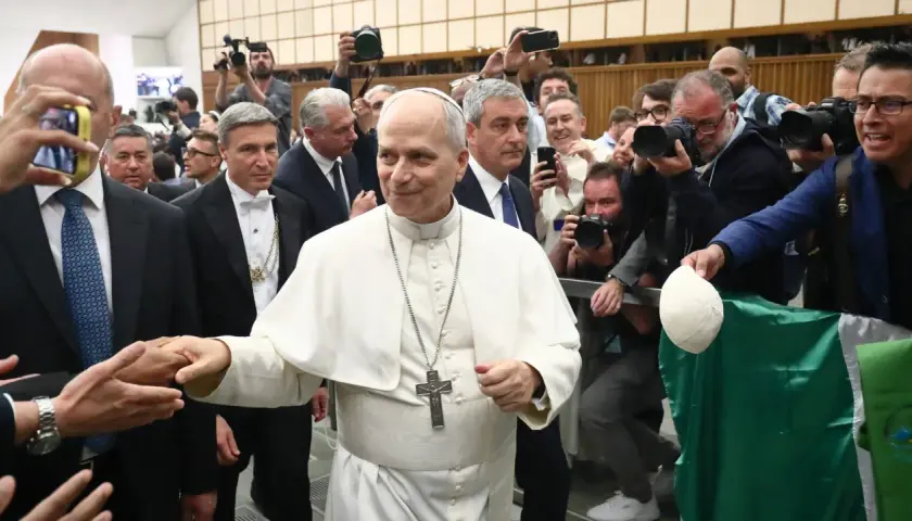 Pius VII, in weißer Soutane, wird von einer Menge umringt, die ihn mit Handys und Kameras fotografiert.