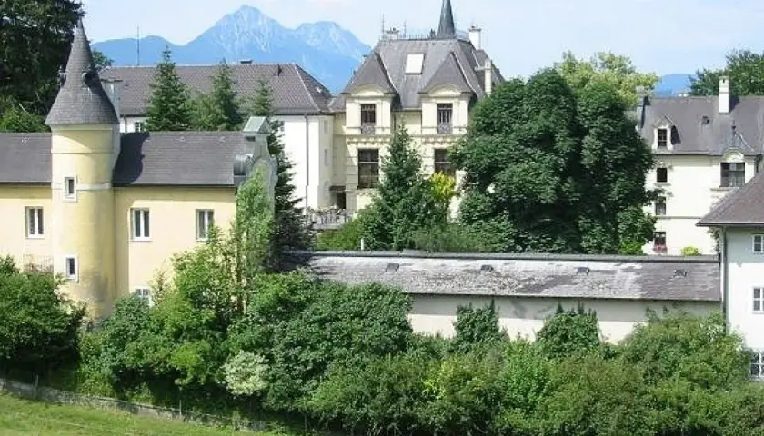 Gelbes Gebäude mit Türmchen und Bergkulisse, erinnert an ein Kloster in Salzburg.