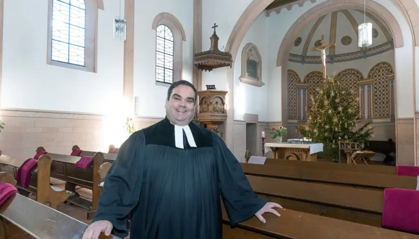 Ein Geistlicher in der Kirche, der die Bänke zeigt. Er wirkt freundlich, als würde er die Bedeutung von Gemeinschaft und Glauben erklären, im Gegensatz zur simonie definition.
