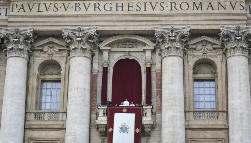 Der Papst steht auf dem Balkon des Petersdoms, umgeben von Kardinälen. Ein großes Wappen hängt über dem Balkon.