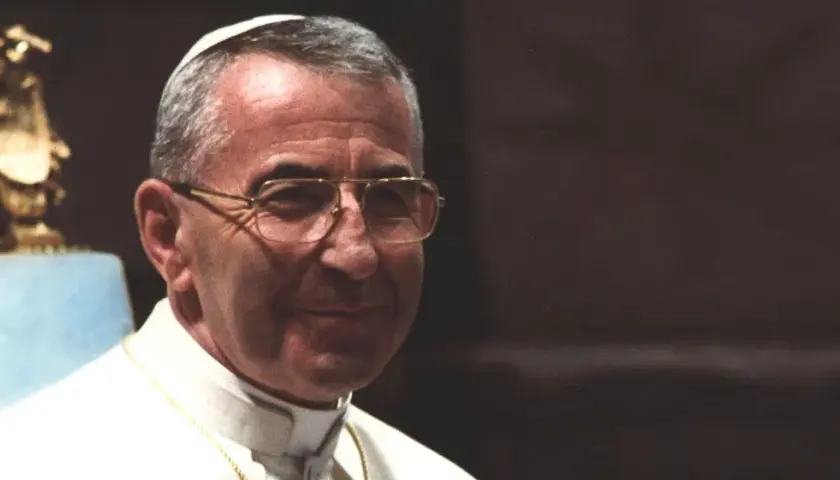 Porträt von Papst Johannes Paul I. mit Brille, im Hintergrund eine goldene Statue.