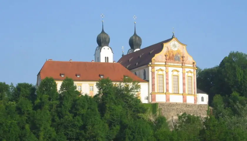 Prachtvolles Kloster Baumburg thront auf einem Hügel, umgeben von üppigem Grün. Zwei markante Zwiebeltürme ragen in den blauen Himmel.
