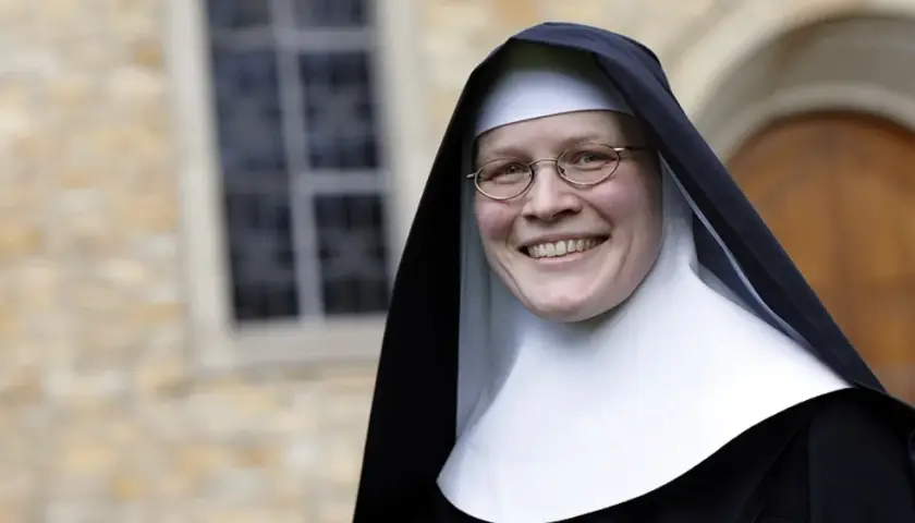 Lächelnde Nonne mit Brille vor einem Kloster. Sie hat sich entschieden, ins Kloster zu gehen und strahlt Zufriedenheit aus.