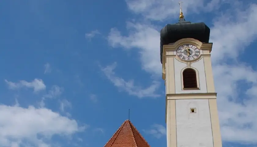 Der Turm der Stadtkirche Bad Aibling ragt in den blauen Himmel mit weißen Wolken.