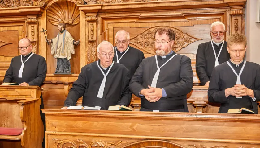 Sechs Geistliche in Soutanen stehen im Chorraum des Stifts Reichersberg.