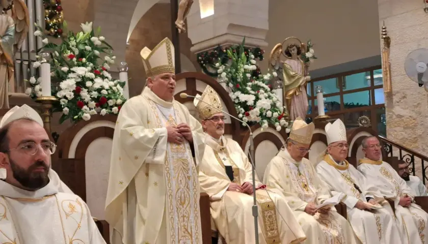 Bischof Konrad Krajewski spricht zu einer Gruppe von Geistlichen in festlicher Kleidung, umgeben von Blumen und religiösen Statuen.