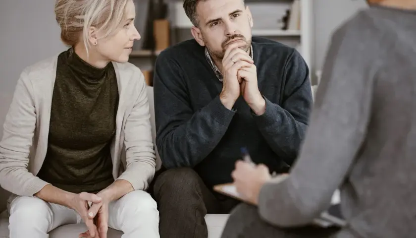 Ein Paar sitzt auf einer Couch und spricht mit einer Person, die Notizen macht. Sie sind in einer Sitzung zur Eheberatung.