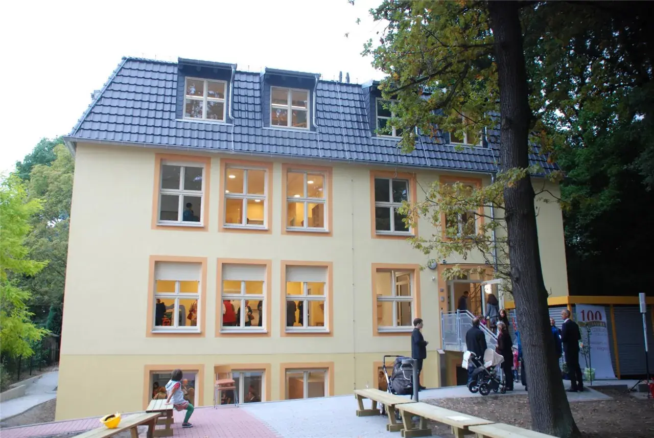 Das Gebäude des Kindergartens St. Klara, ein hellgelbes Haus mit vielen Fenstern, lädt zum Spielen ein.