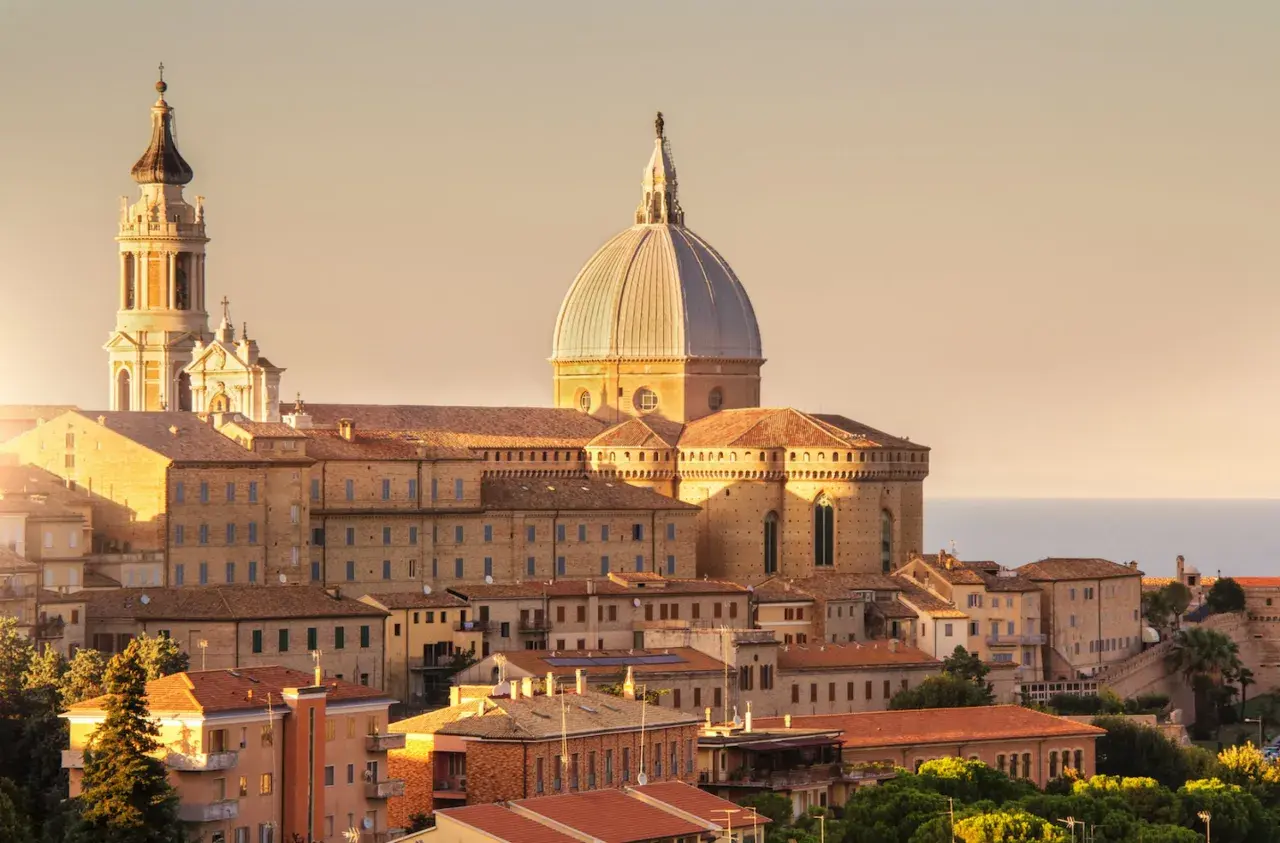 Sonnenuntergang über der Basilika von Loreto, Italien. Die Kuppel und der Glockenturm ragen über die Dächer der Stadt auf.