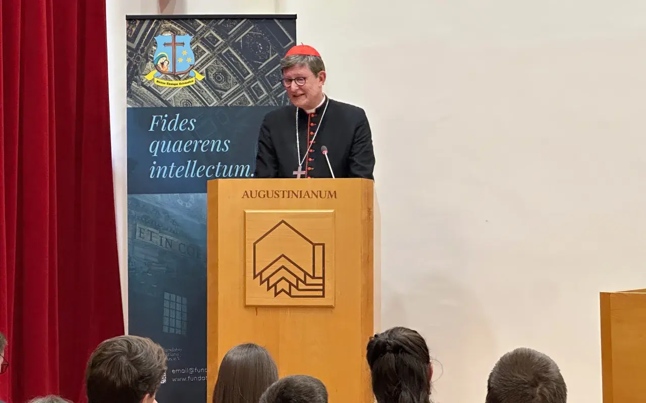 Kardinal Woelki spricht vor Zuhörern im Augustinianum. Er trägt eine schwarze Soutane und einen roten Pileolus.