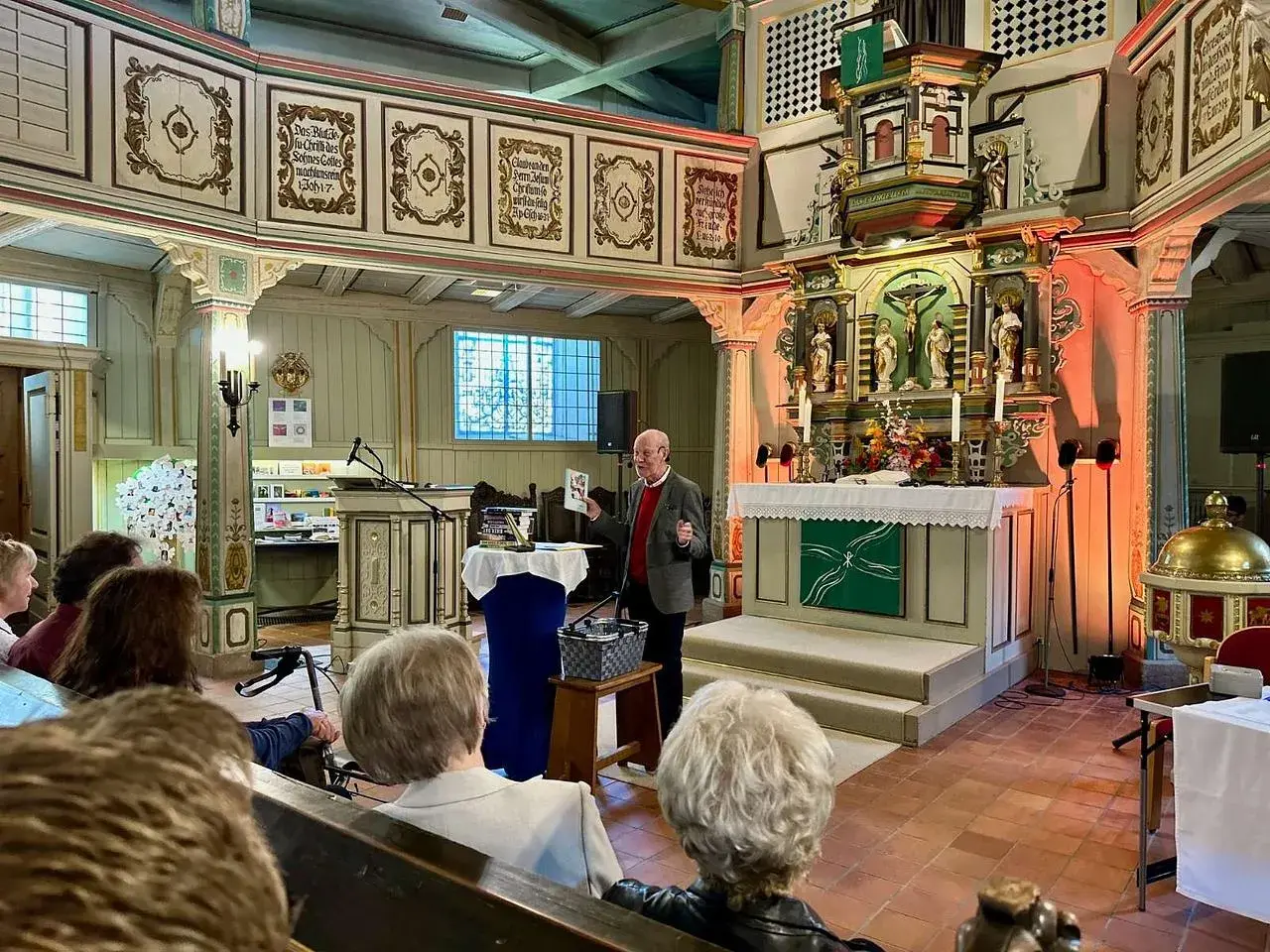 Ein Mann spricht in einer Kirche vor Zuhörern. Er hält ein Buch hoch, das von seelischem Widerstand handeln könnte.