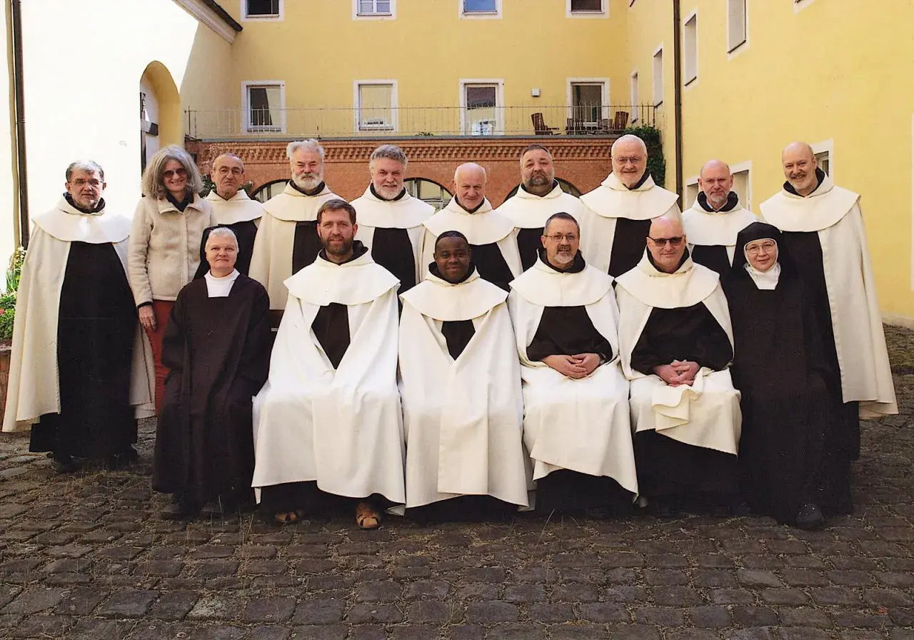 Gruppe von unbeschuhten Karmeliten in braunen Kutten und weißen Umhängen posiert vor einem gelben Gebäude.