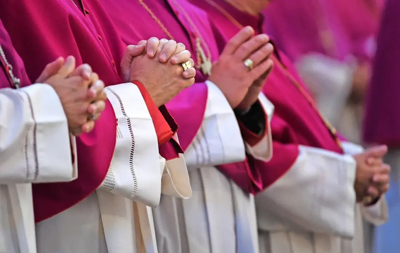 Geistliche in violetten Roben beten. Auch ein Pfarrer zahlt Kirchensteuer, wie die Ringe an den Fingern zeigen.