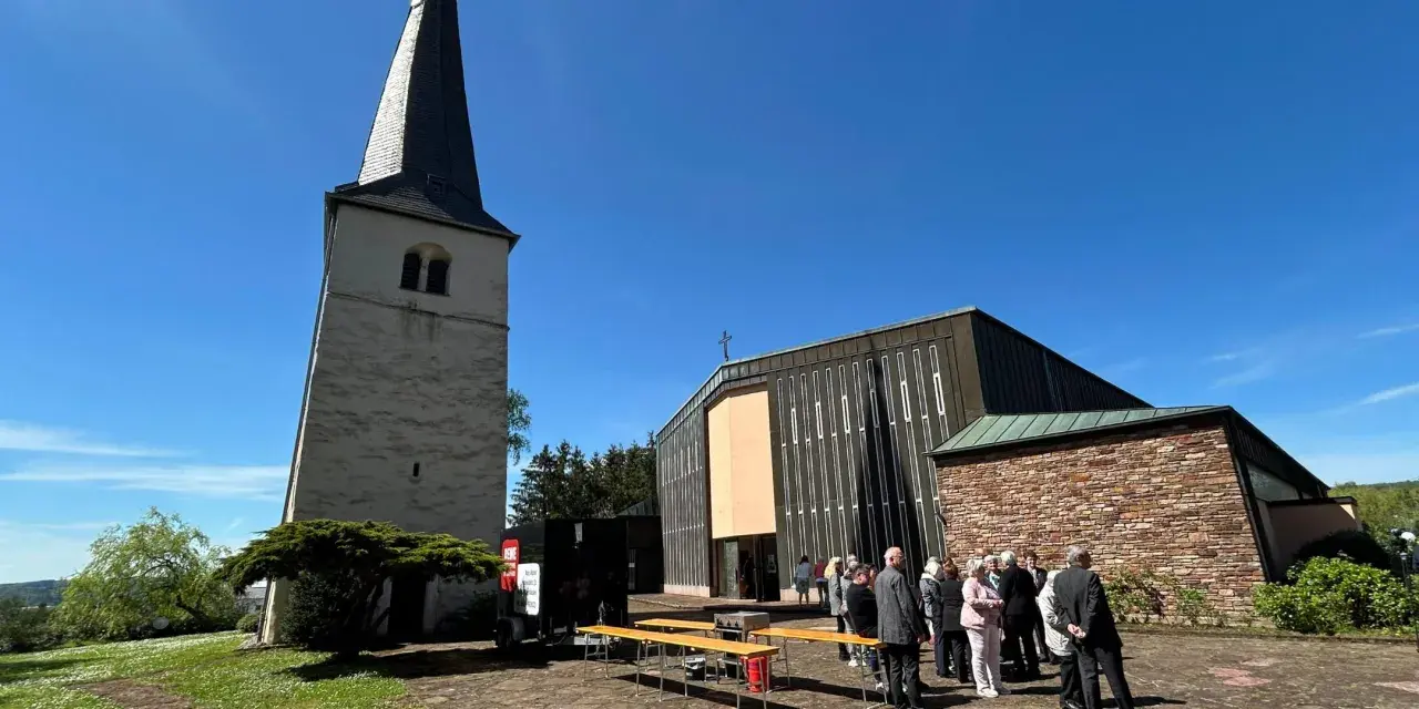 Menschen versammeln sich vor einer Kirche mit einem alten Turm. Die Frage "was ist Profanierung" könnte hier aufkommen, wenn die Kirche nicht mehr als Gotteshaus genutzt wird.