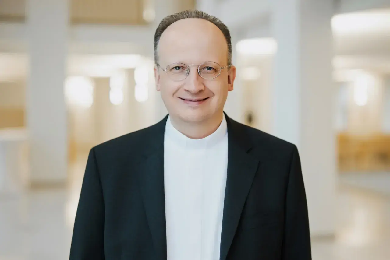 Ein Mann mit Brille trägt ein schwarzes Sakko über einem weißen Hemdkragen. Er lächelt freundlich. Er könnte ein Generalvikar sein, der die Stellvertretung des Bischofs übernimmt.