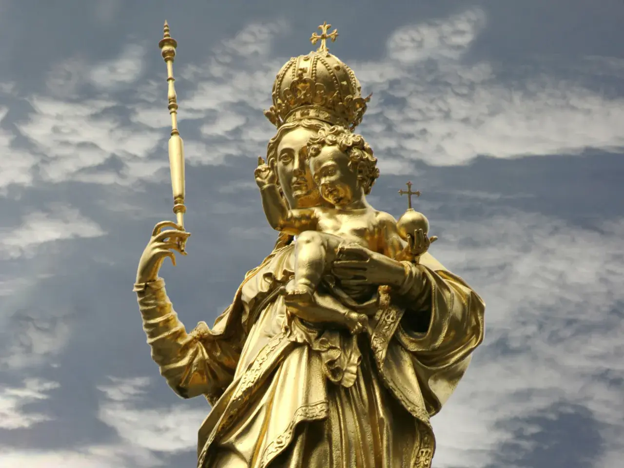 Goldene Statue der Muttergottes mit Kind, dem Patron von Bayern, vor dramatischem Wolkenhimmel.
