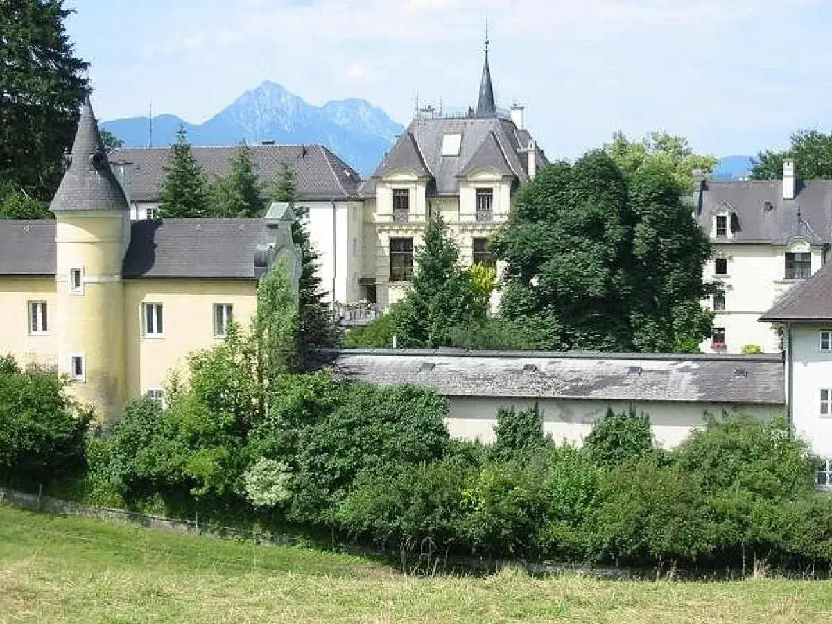 Gelbes Gebäude mit Türmchen und Bergkulisse, erinnert an ein Kloster in Salzburg.