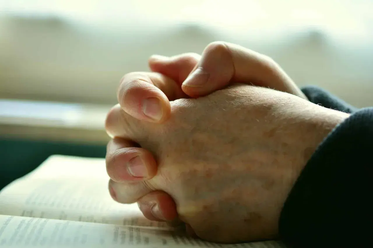 Gefaltete Hände über einem Buch, ein Zeichen von Glauben und dem Ringen mit **Gott und dem Leid**.