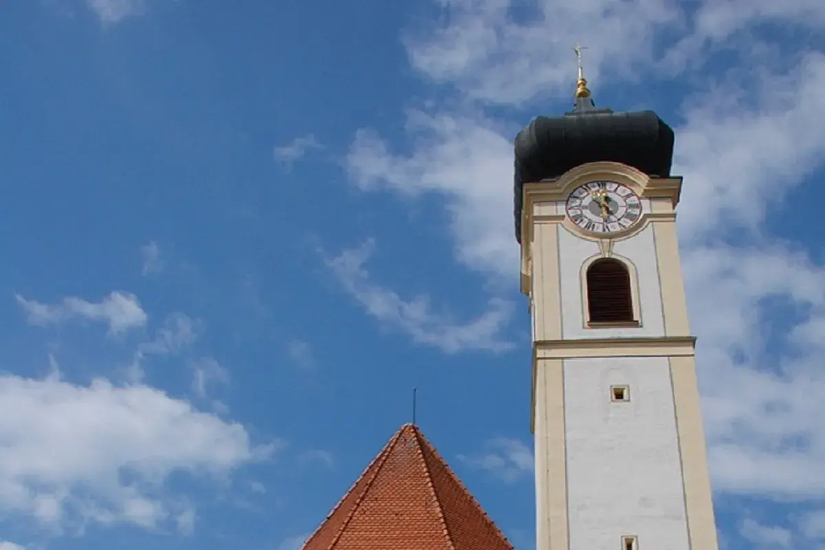 Der Turm der Stadtkirche Bad Aibling ragt in den blauen Himmel mit weißen Wolken.
