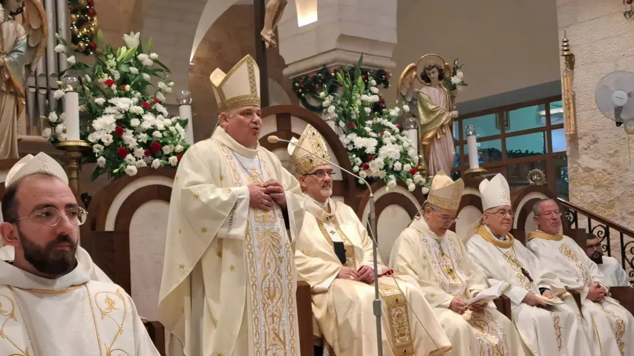 Bischof Konrad Krajewski spricht zu einer Gruppe von Geistlichen in festlicher Kleidung, umgeben von Blumen und religiösen Statuen.