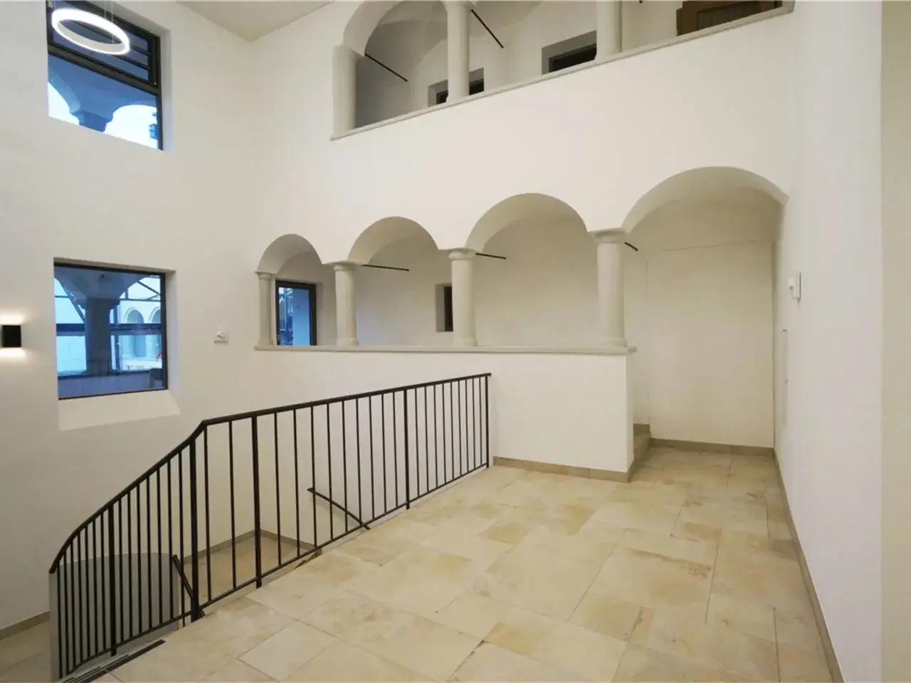 Innenansicht des bischof bernhard haus kraiburg mit einer geschwungenen Treppe, B&ouml;gen und S&auml;ulen.