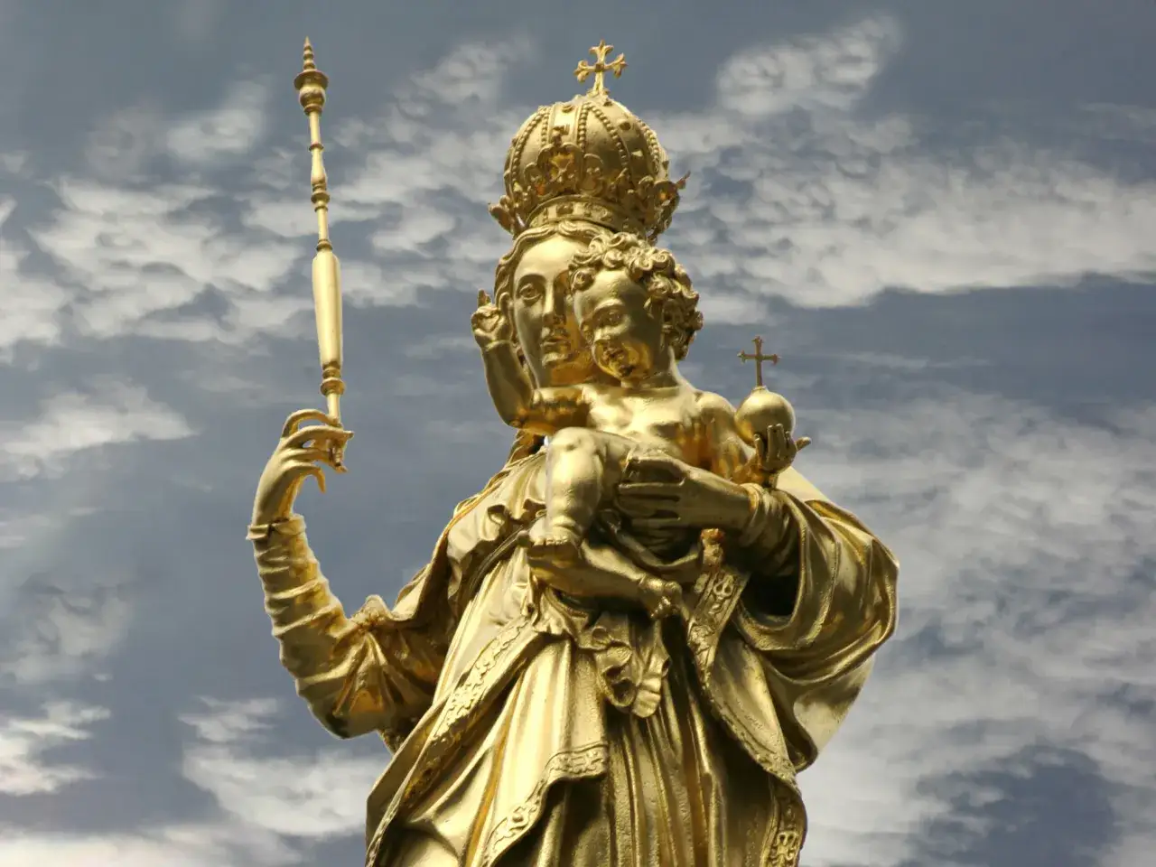 Goldene Statue der Muttergottes mit Kind, dem Patron von Bayern, vor dramatischem Himmel.