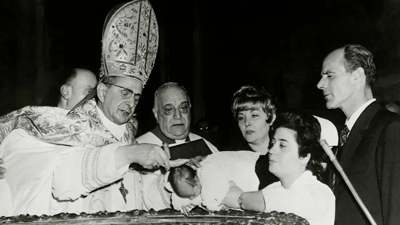 Papst Paul VI. tauft ein Baby. Eine Frau h&auml;lt das Kind, w&auml;hrend ein Mann daneben steht.