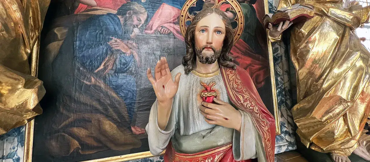 Statue des heiligstes Herz Jesu mit Wundmalen, daneben eine goldene Figur und ein Gemälde.