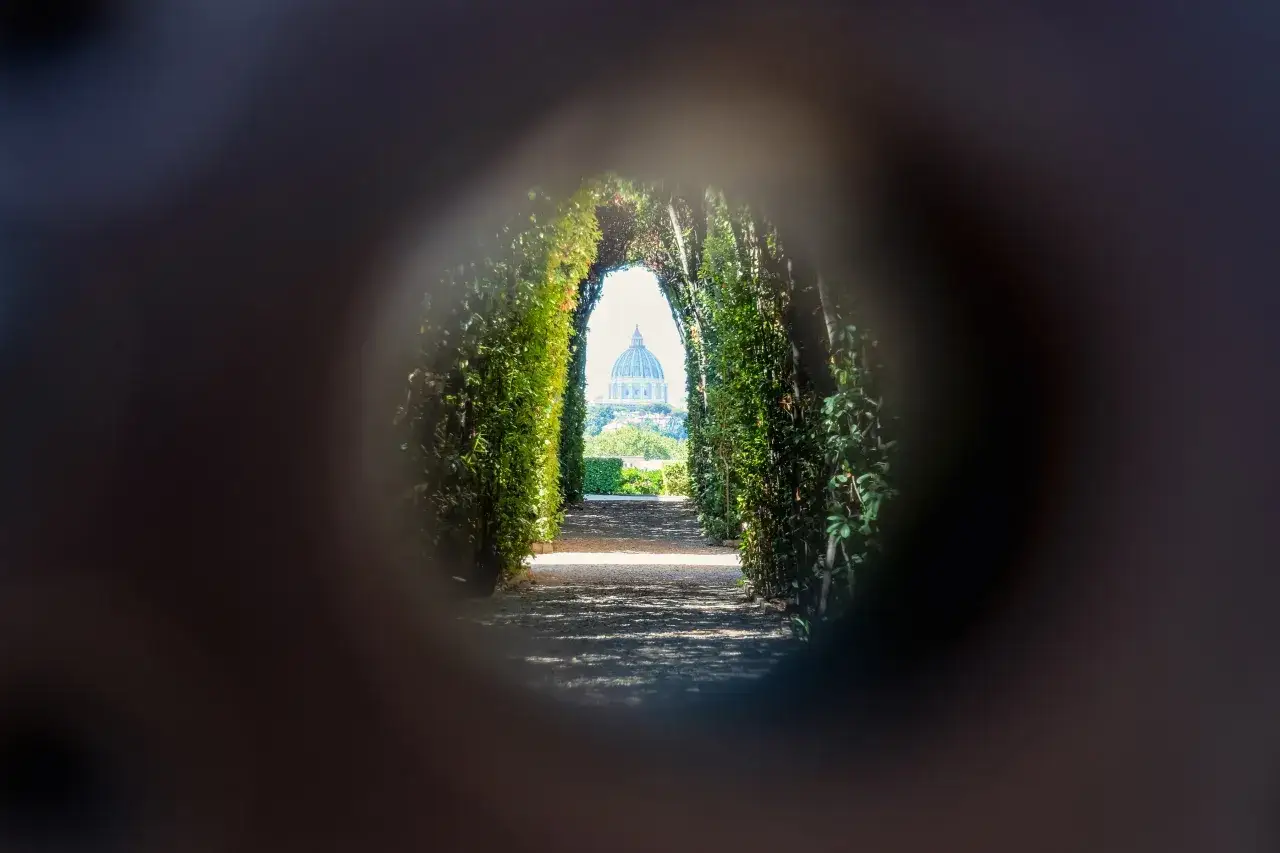 Blick durch einen gr&uuml;nen Torbogen auf die Kuppel des Petersdoms in Rom. Ein versteckter Pfad, der an den Malteser Orden in Rom erinnert.