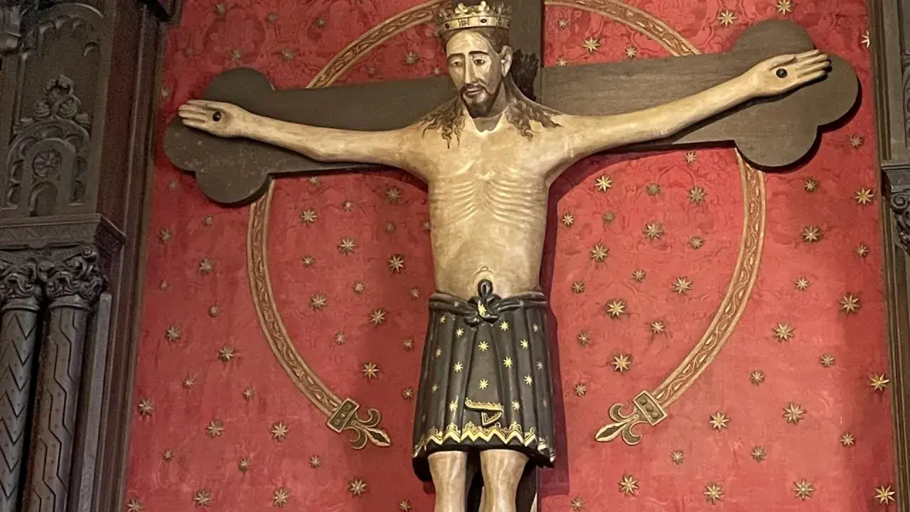 Holzschnitzerei des Splitters vom Kreuz Jesu mit Dornenkrone und Lendentuch vor rotem Hintergrund mit goldenen Sternen.