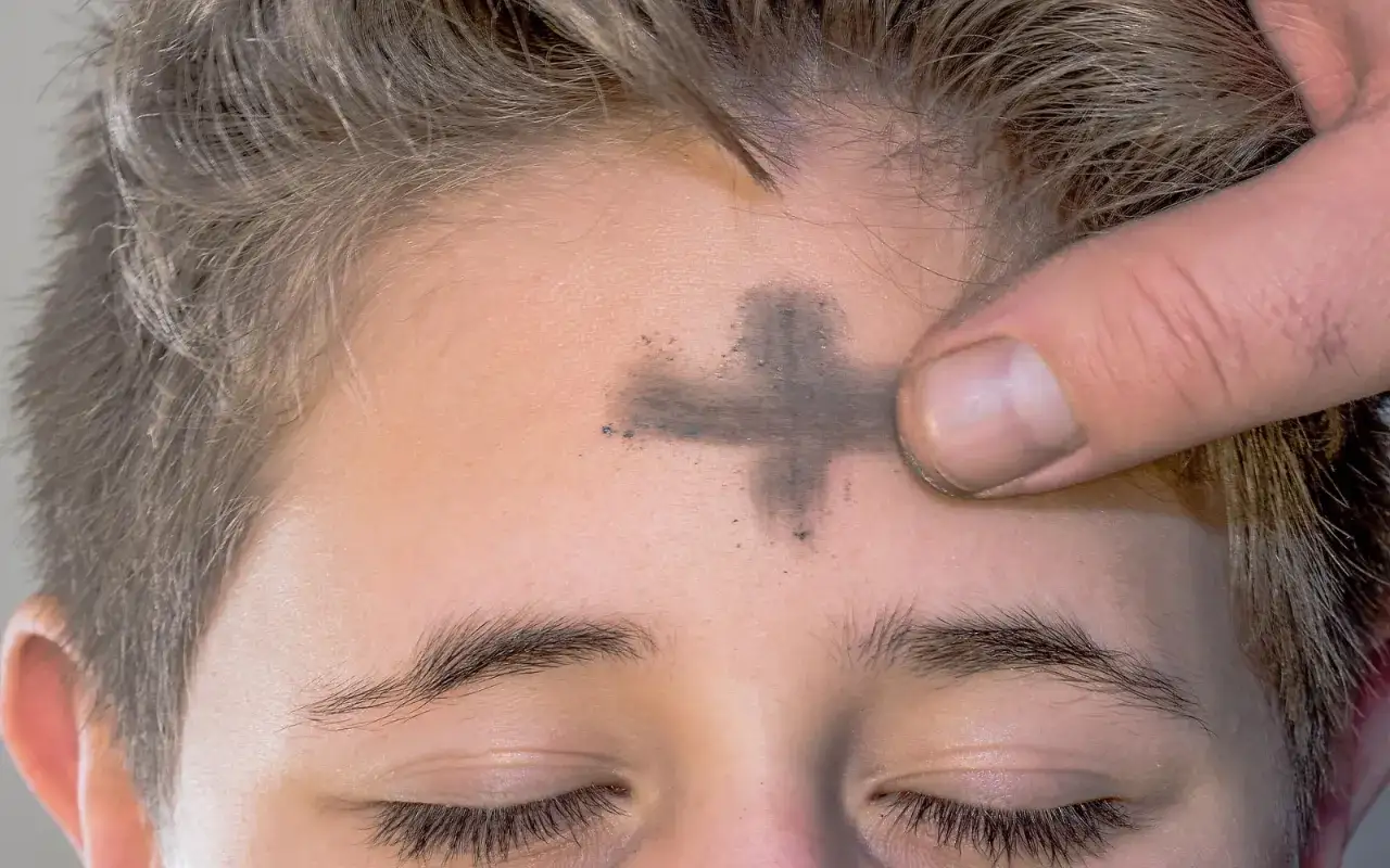 Ein Finger zeichnet ein Aschekreuz auf die Stirn eines Kindes. 