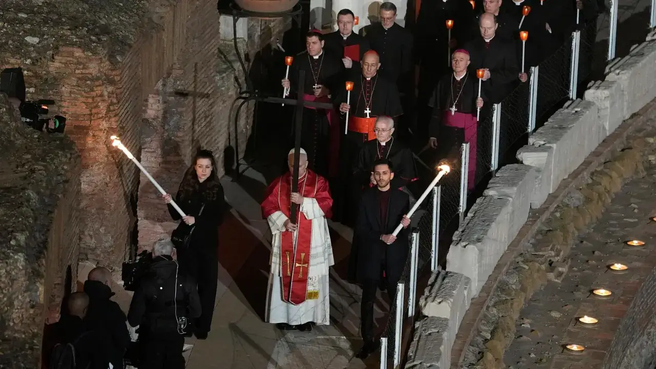 Papst Franziskus trägt ein Kreuz bei einer Prozession, die an die Passion Christi erinnert. Geistliche und Gläubige mit Fackeln und Kerzen begleiten ihn.