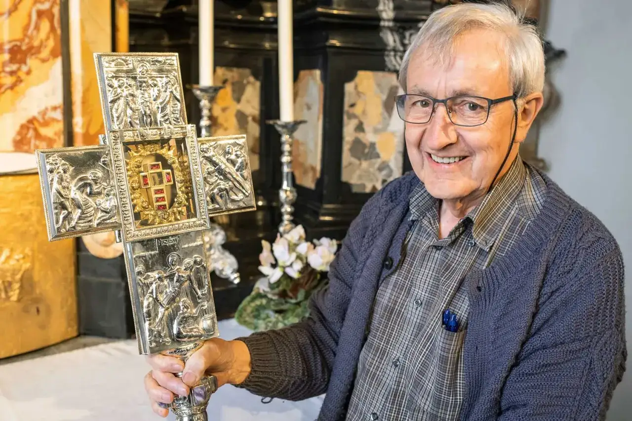 Ein Mann h&auml;lt ein kunstvoll verziertes, silbernes Jesus-Kreuz-Original mit Reliefs und roten Steinen.