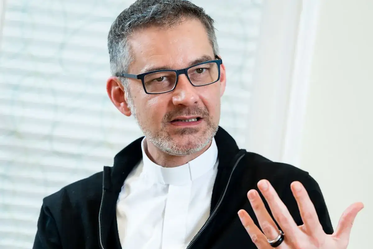 Ein Mann mit Brille und Klerikalkragen spricht. Er erklärt, was ein Generalvikar ist, und gestikuliert dabei.