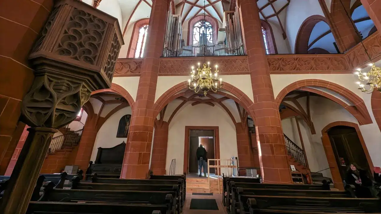 Im Inneren der Kirche St. Leonhard: Orgel, Kronleuchter, Bänke und eine Person am Eingang.