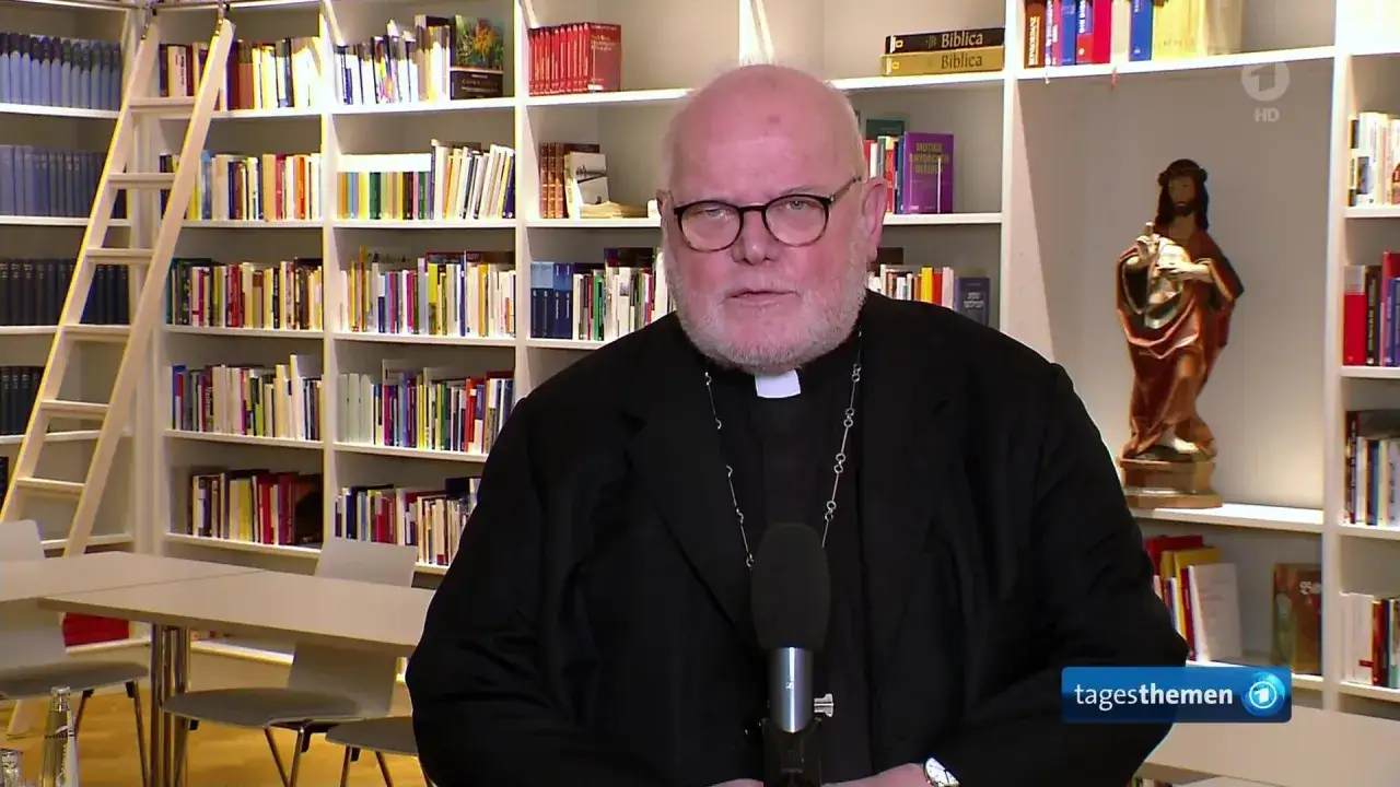 Reinhard Marx, Kardinal, spricht vor einem Bücherregal. Eine Jesus-Statue steht auf einem Regal.