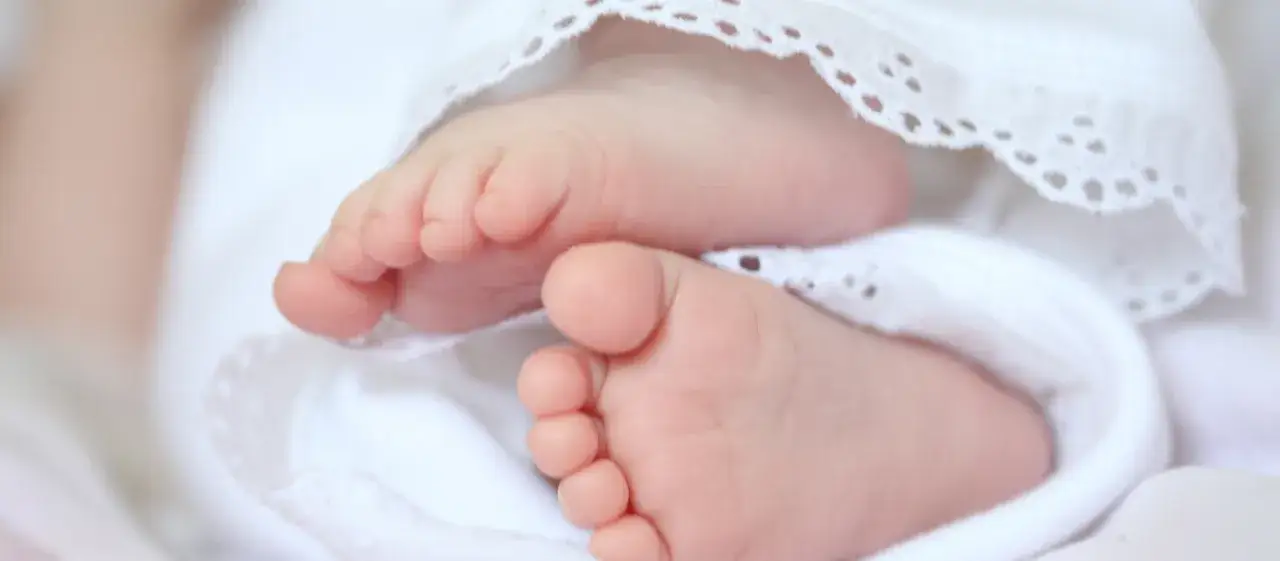 Zarte F&uuml;&szlig;chen eines Babys, umh&uuml;llt von wei&szlig;er Spitze. Vielleicht ein Name wie Maria oder Anna, katholische heilige Namen weiblich, f&uuml;r dieses kleine Wunder.